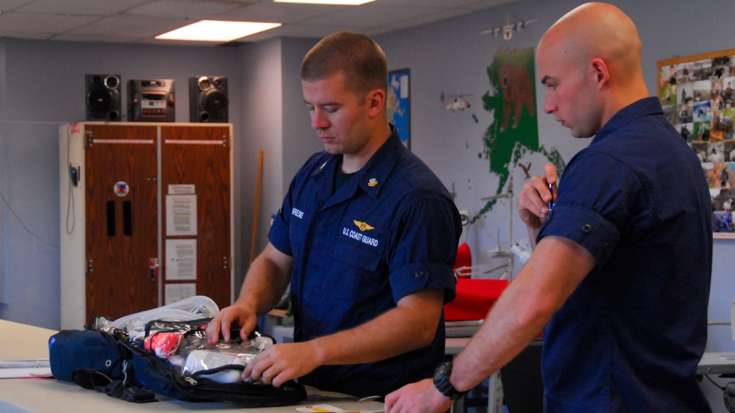 Two Coast Guard technicians inspect emergency medical supplies inside an open equipment bag