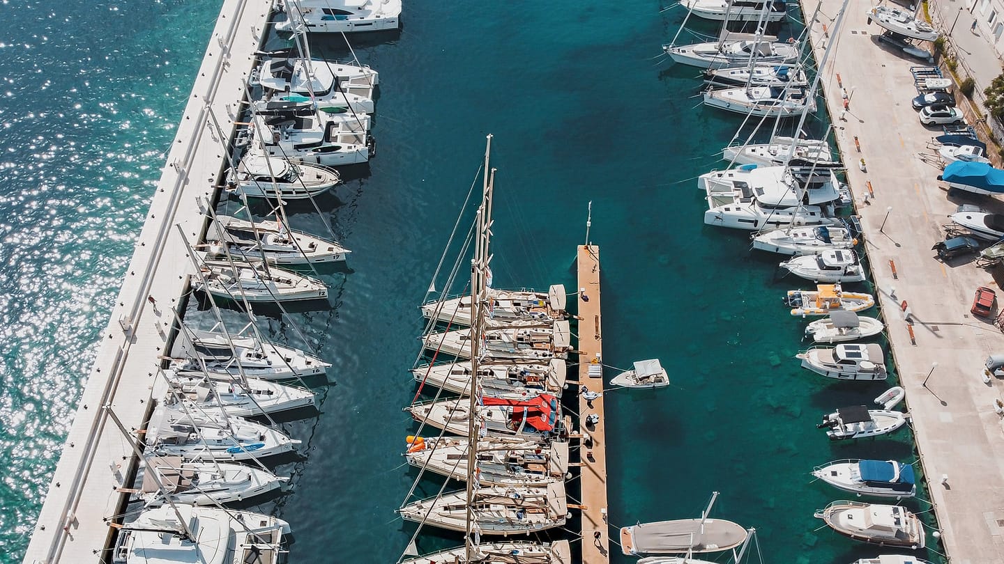An aerial view shows sailboats moored in clear marina water.