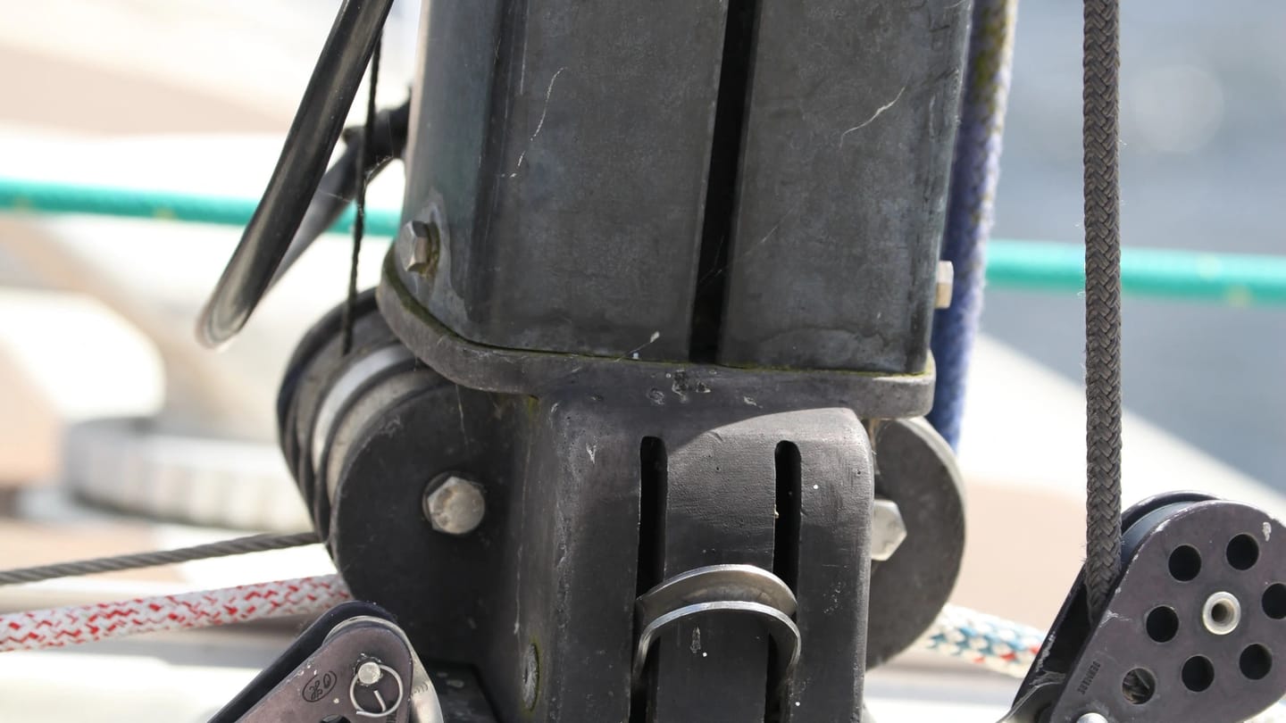 Black deck-stepped sailboat mast heel seated in its metal step, with turning blocks and electrical cables visible.