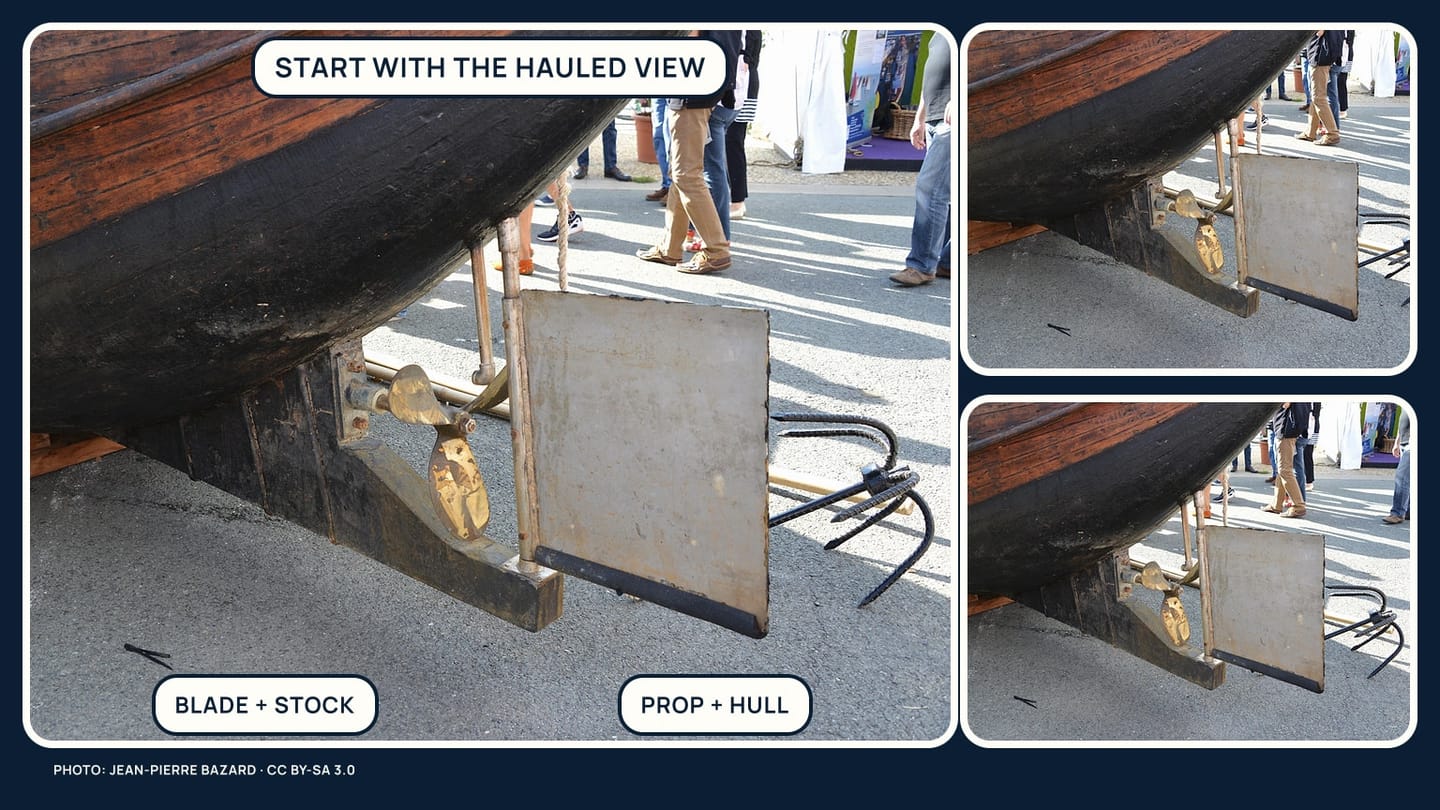 A hauled sailboat rudder photographed with its blade, stock area, propeller, and hull context