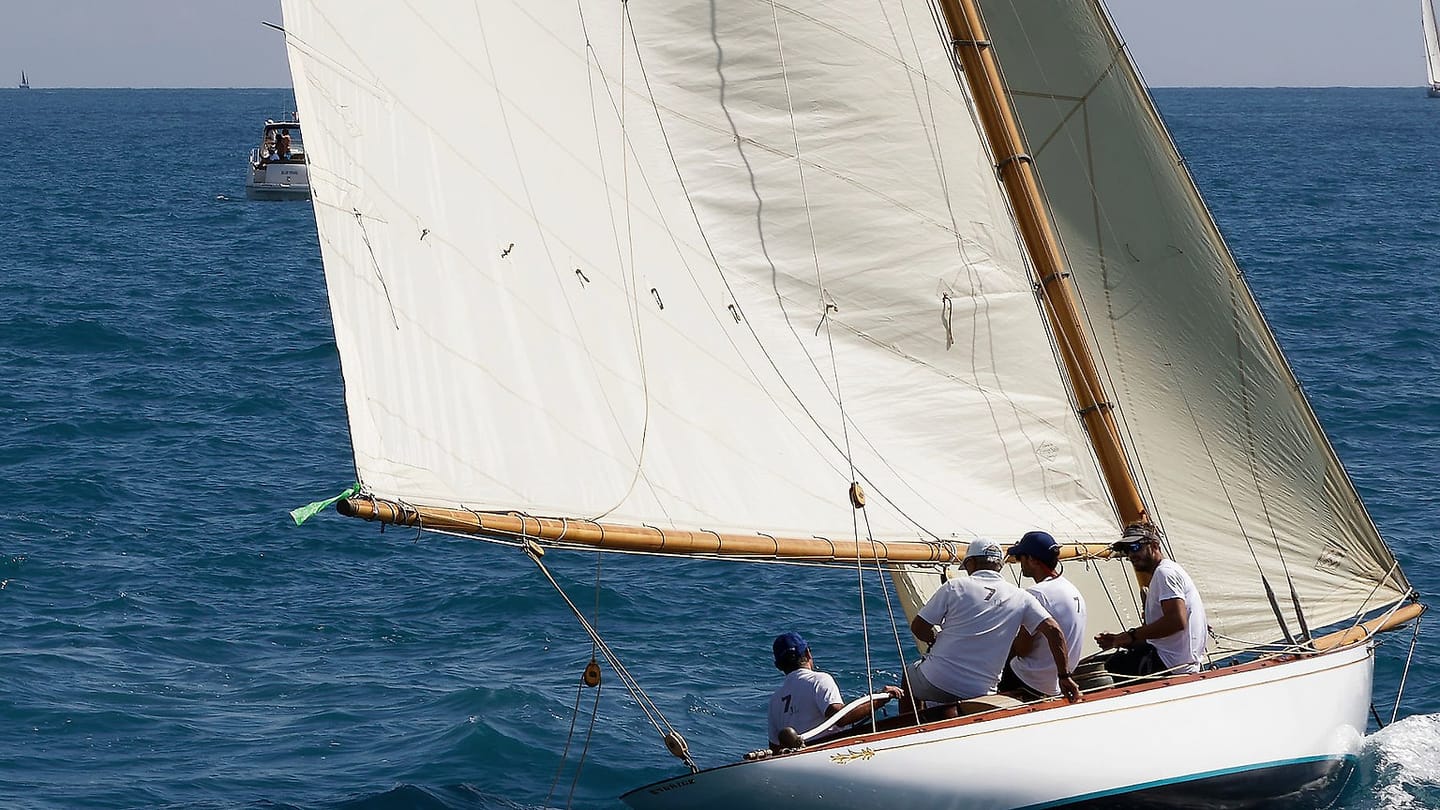 A sailing crew operates a yacht on open water in daylight.