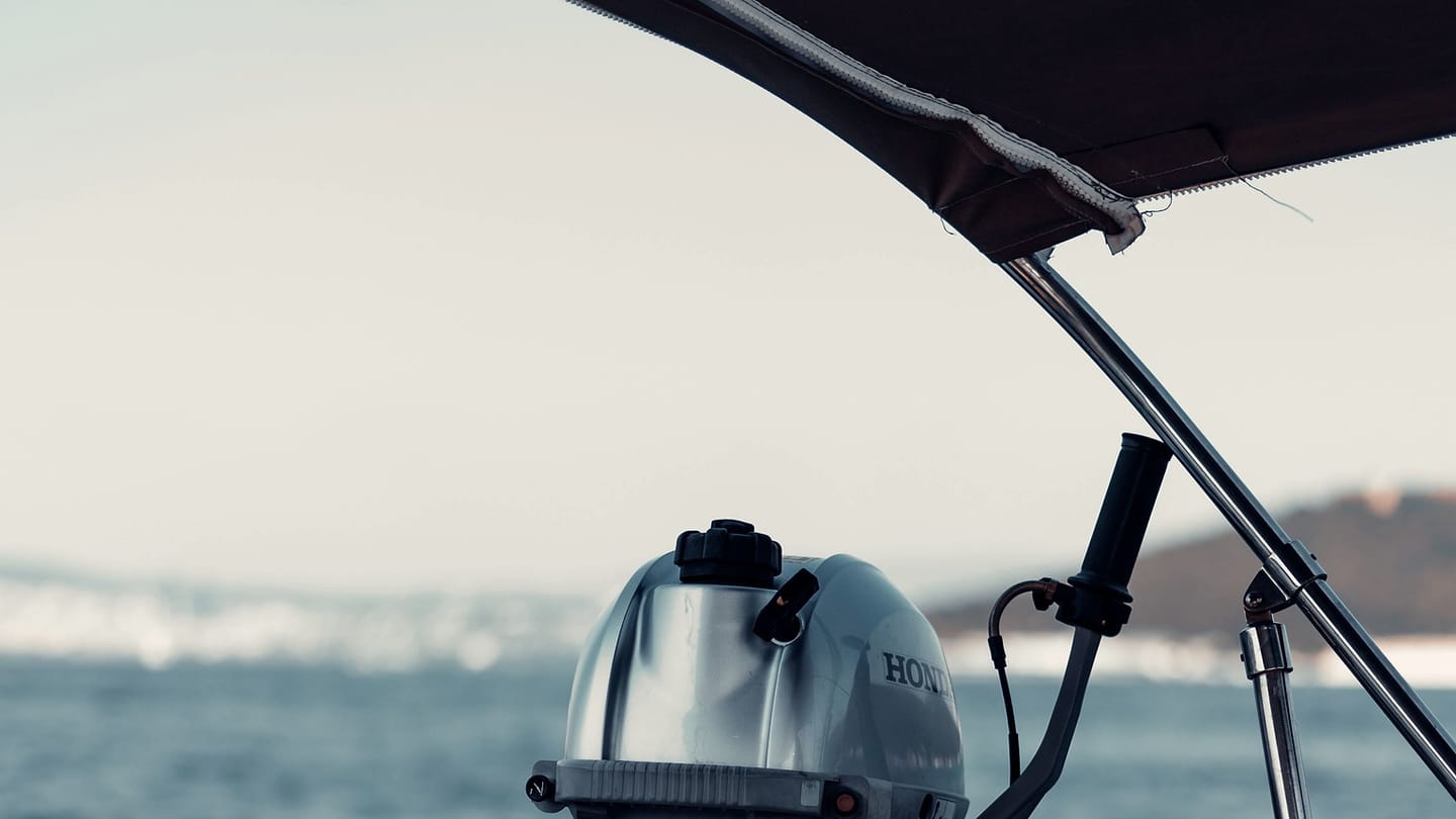 An outboard motor, control cable, and mounting bracket are visible at a boat stern.