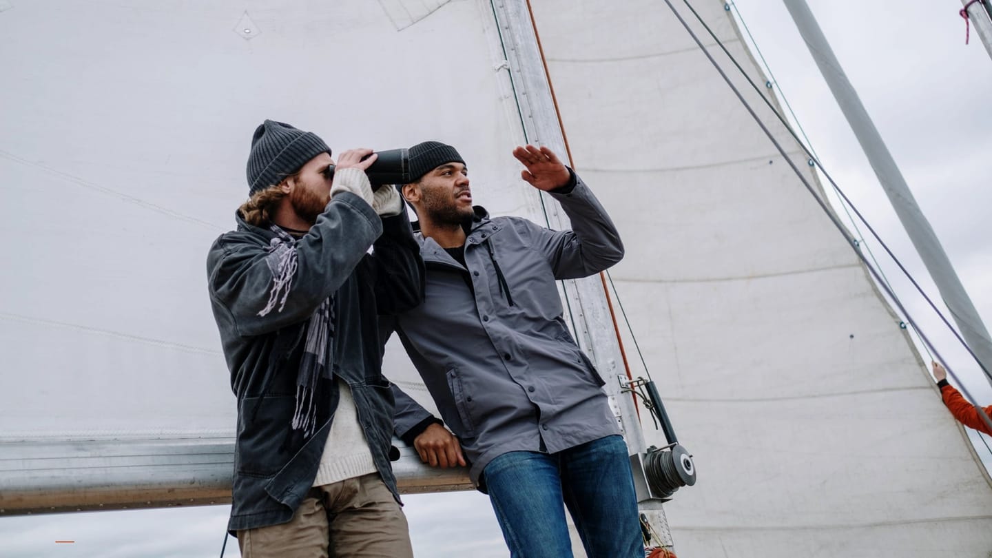 Crew member listening while a partner speaks beside the sail
