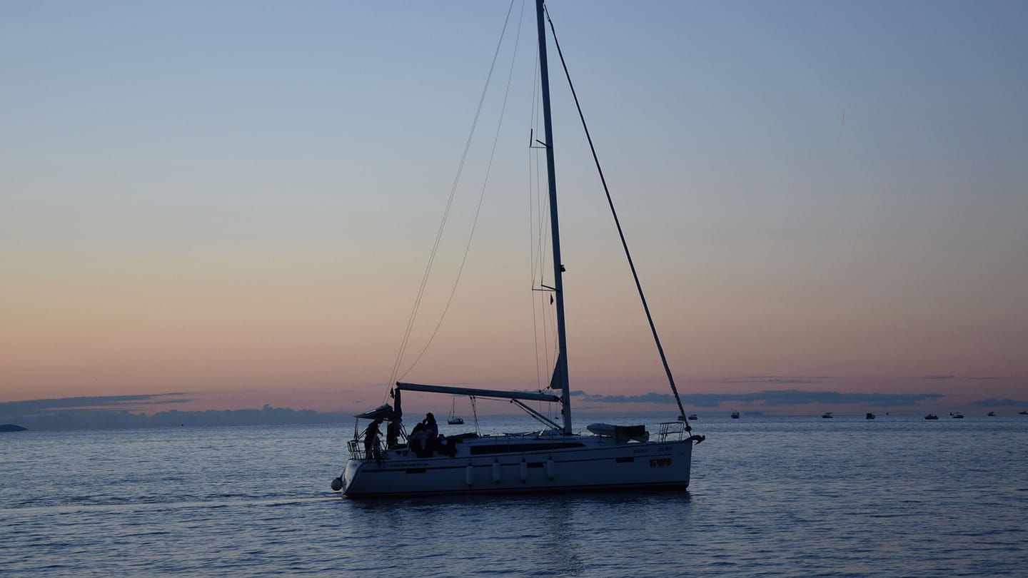 A sailboat silhouette against the last light of dusk shows how quickly shape gives way to lights.