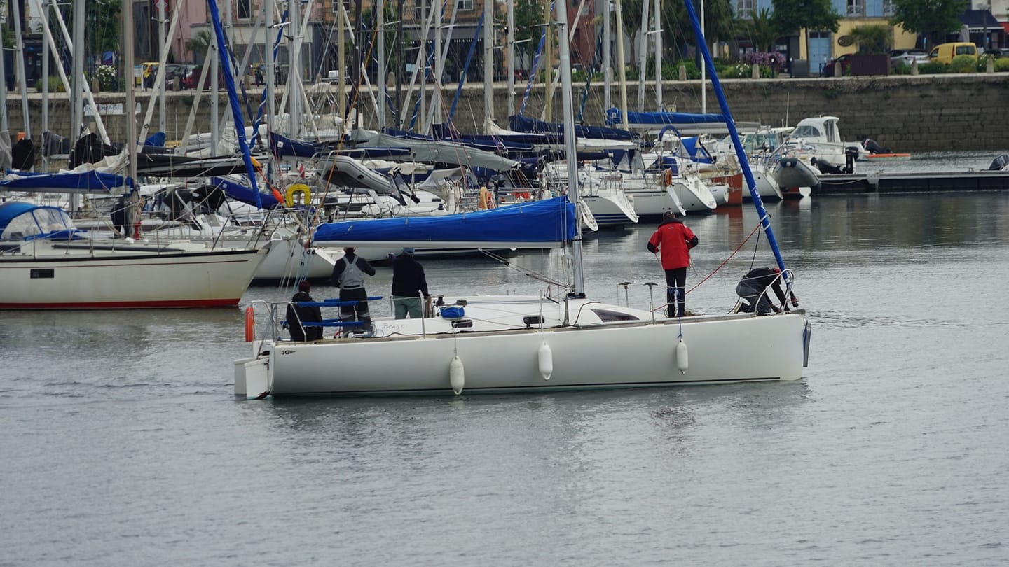 People preparing a sailboat beside a busy marina