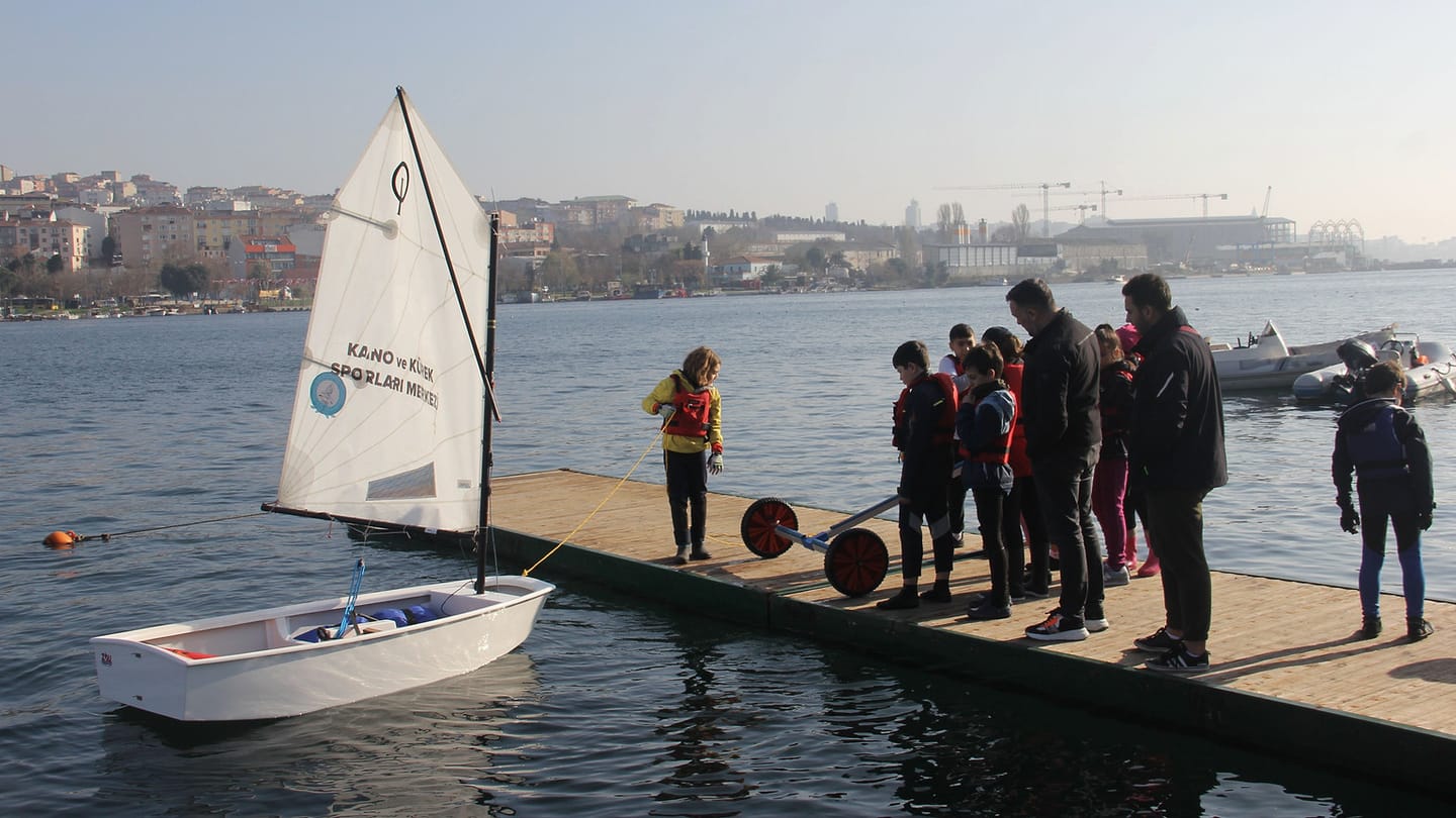 A group in life jackets gathered beside a small sailing dinghy