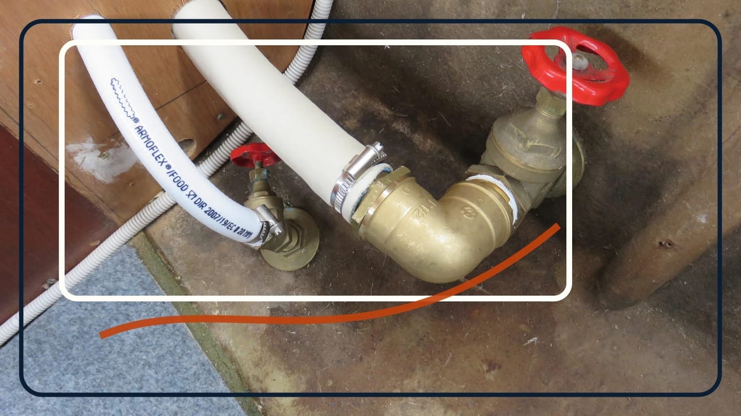 Two bronze seacocks with red handles connected to white hoses inside a brown fiberglass compartment.