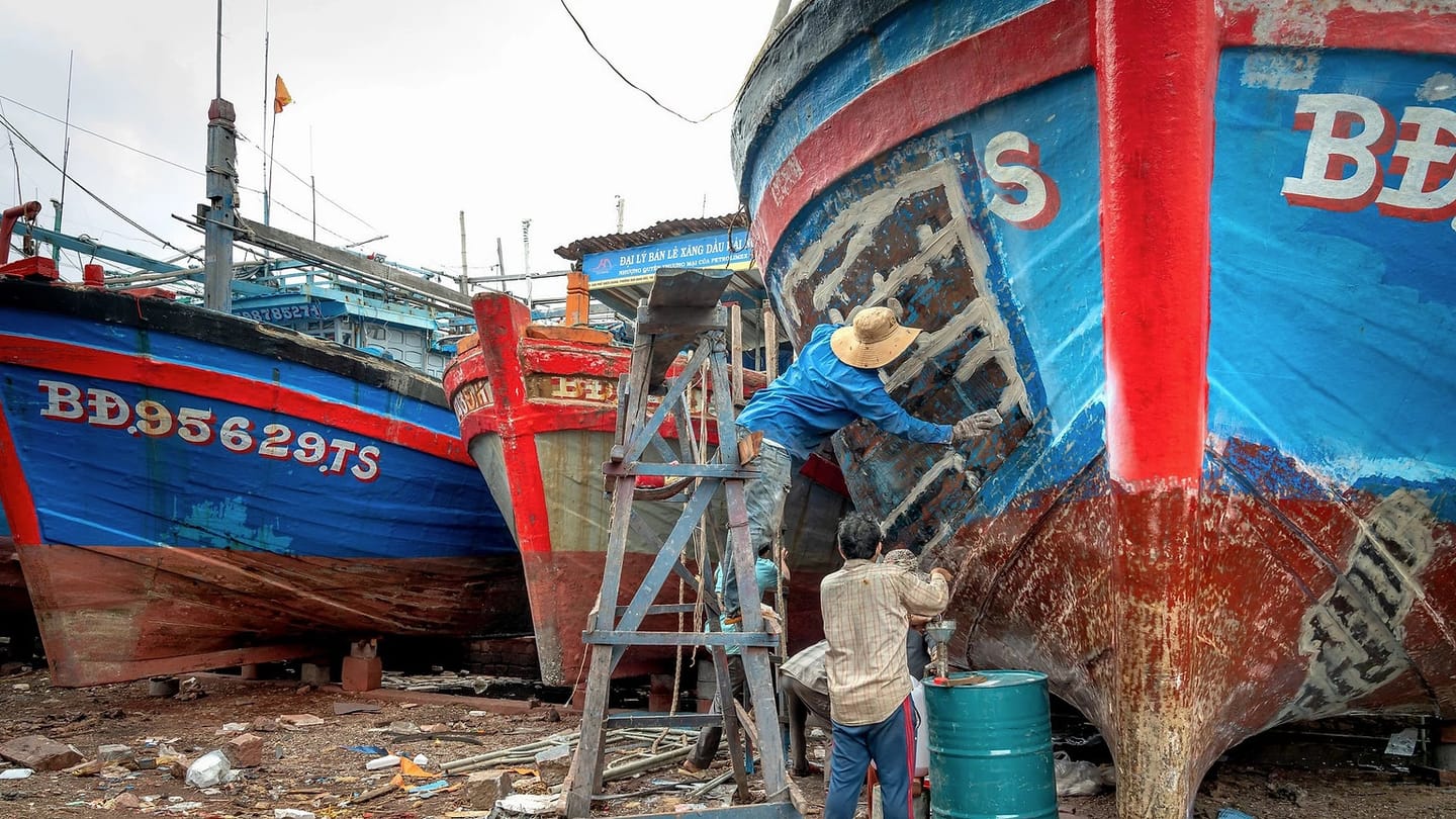 Workers repairing a boat hull in a yard