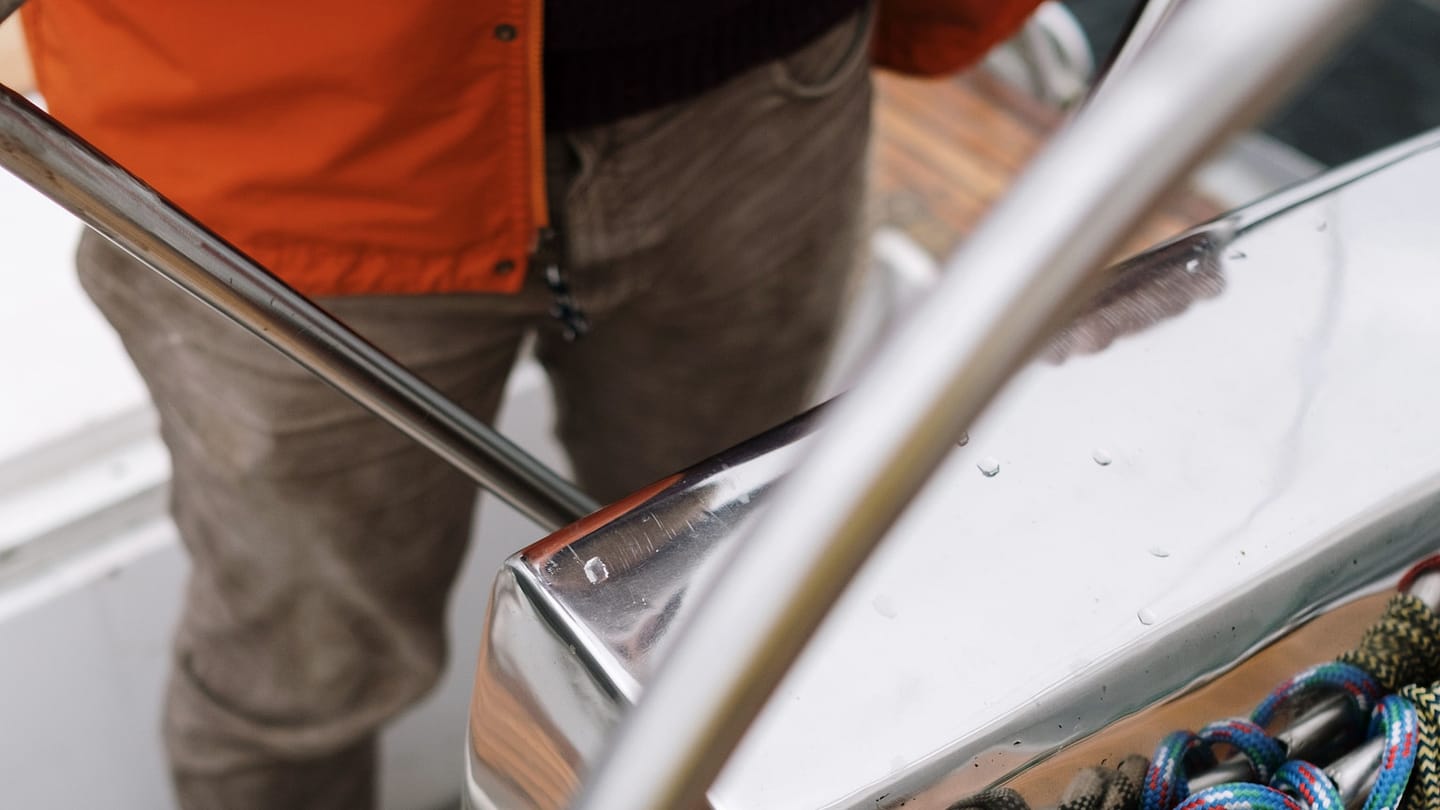 A sailor holds the wheel at the helm of a sailing yacht.
