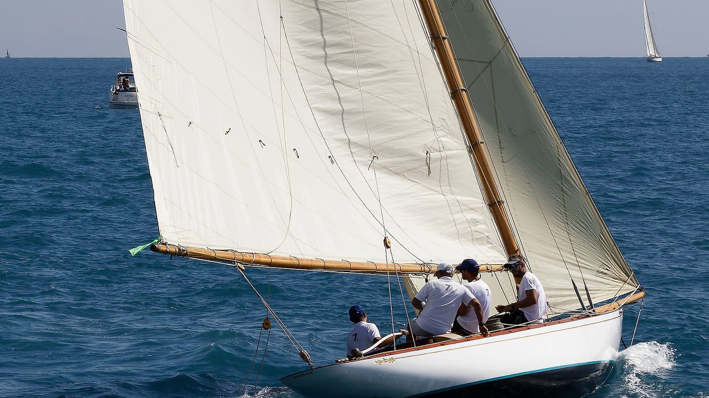 Sailors sit around the cockpit of a yacht moving through open water.