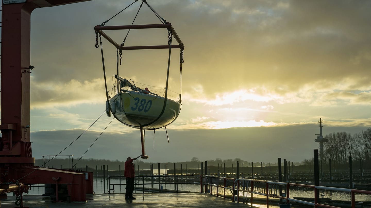 A sailboat stands ashore near harbor lifting equipment and water.