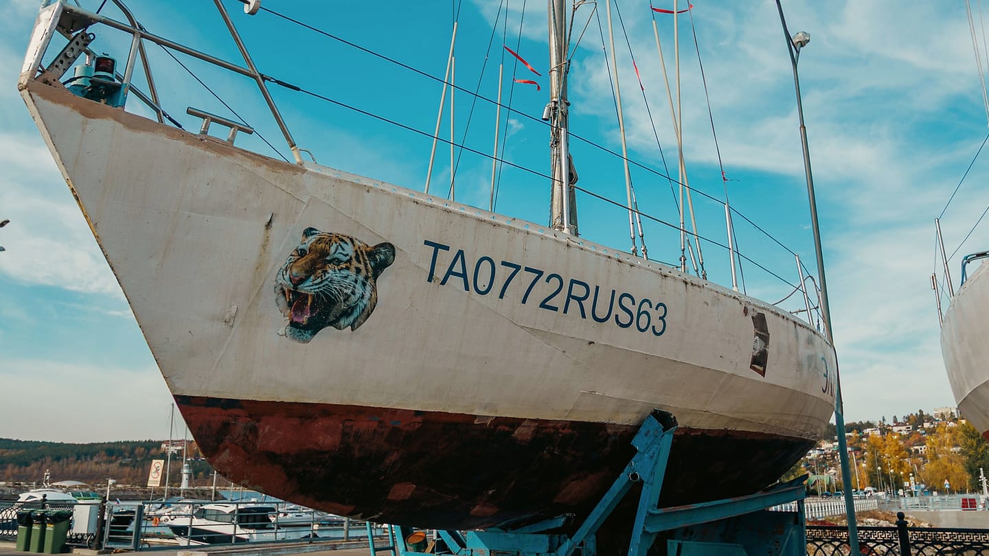 A sailboat stands ashore with its hull, keel, mast, and support frame visible.