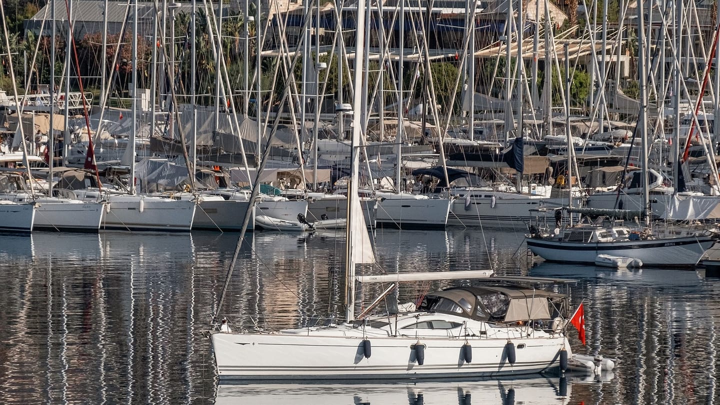 A sailboat moves through the fairway between two marina docks.