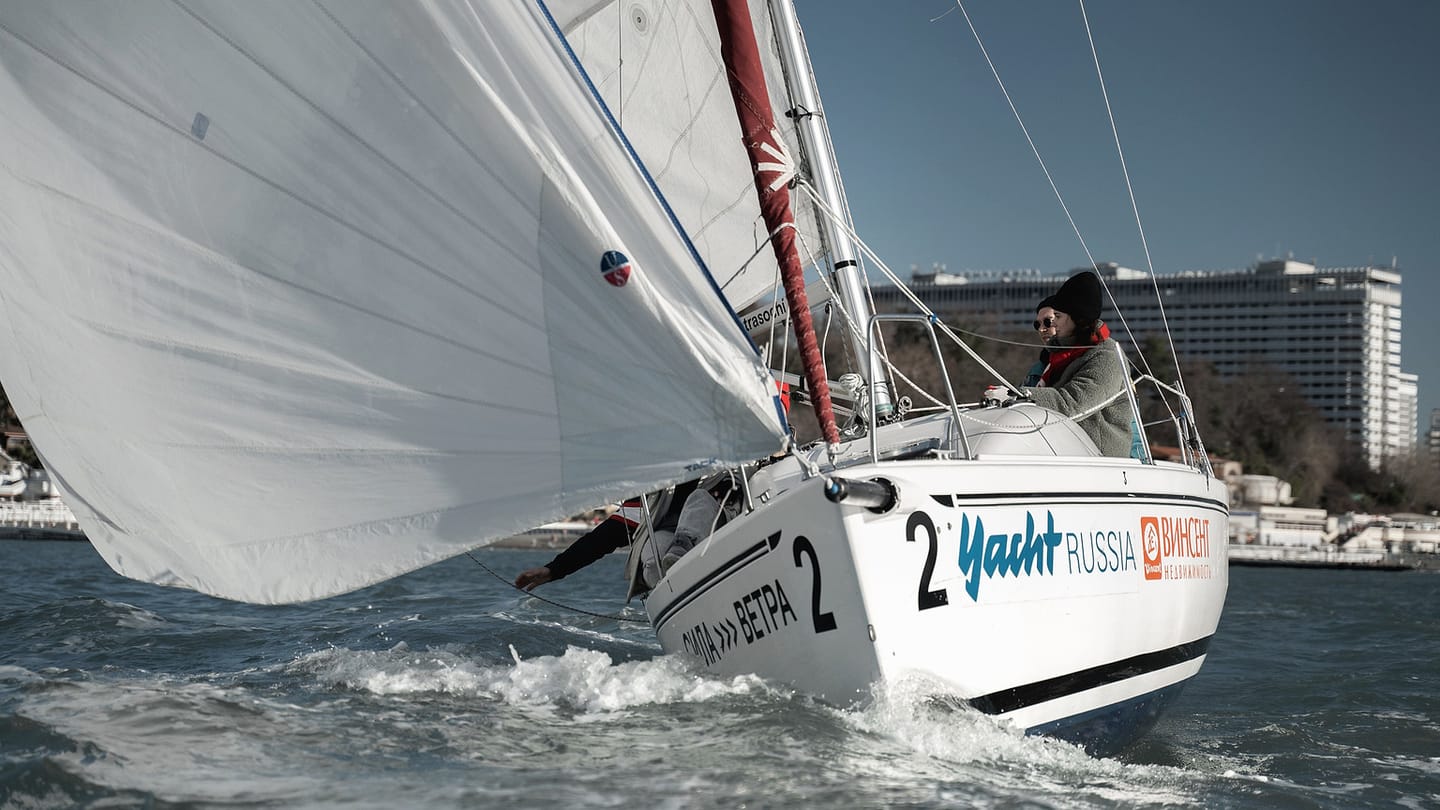 A sailor steers a heeled sailboat from the cockpit.