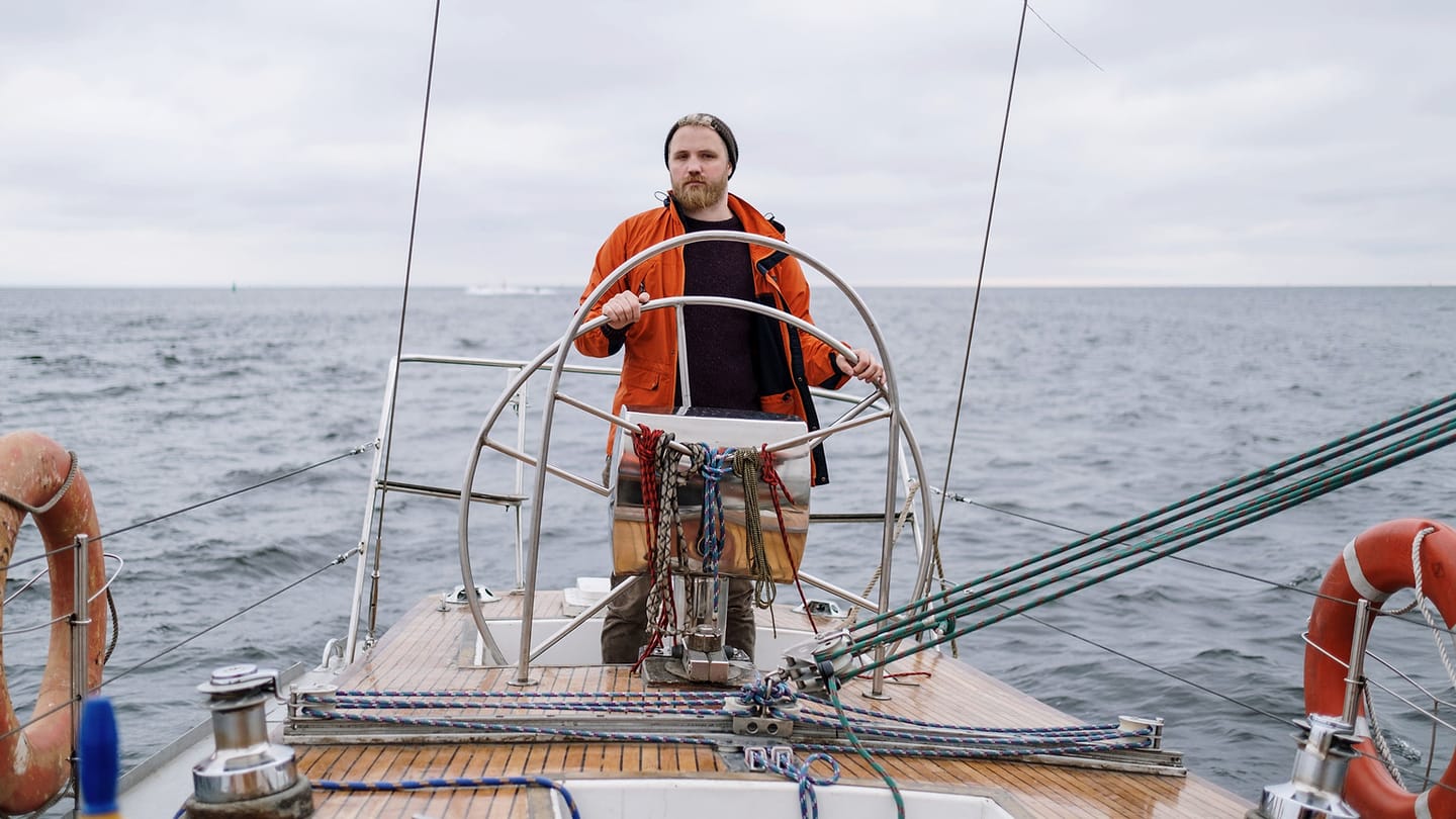 A crew member works with a line beside the mainsail during a trim adjustment.
